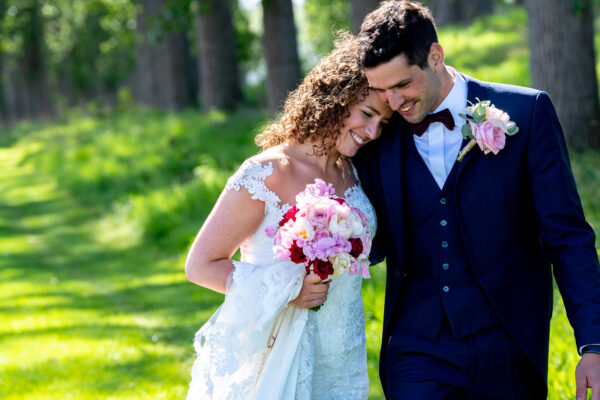 Een trouwkoppel op hun huwelijksdag in de lentezon en een boeket bloemen in de hand.